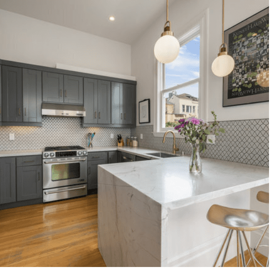 Kitchen with gray cabinetry, marble island, brass faucet, and globe pendant lighting.